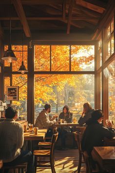 people sitting at tables in a restaurant with autumn leaves on the trees out front window