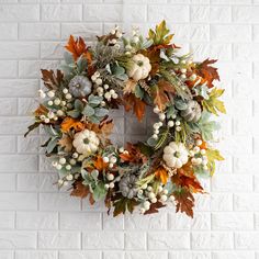 a wreath with white pumpkins and green leaves on a brick wall in front of it