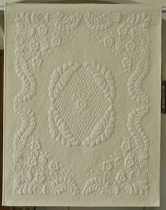 a white quilt hanging on the wall with an intricate design in it's center