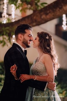 a man and woman standing next to each other in front of a tree with lights