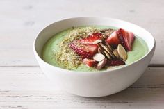 a white bowl filled with green smoothie topped with strawberries and almonds on top