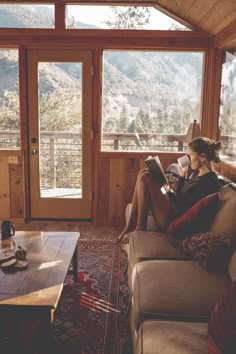 a woman sitting on top of a couch in front of a window reading a book