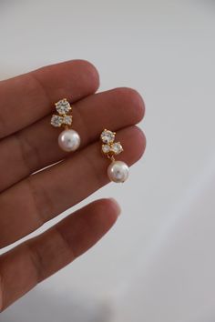 a hand holding two pearl and diamond earrings