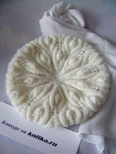 a white knitted hat sitting on top of a bed next to a paper napkin