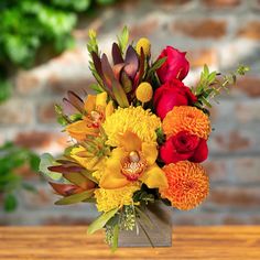 a vase filled with lots of colorful flowers on top of a wooden table next to a brick wall