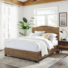 a bed with white linens and pillows in a room next to a large potted plant