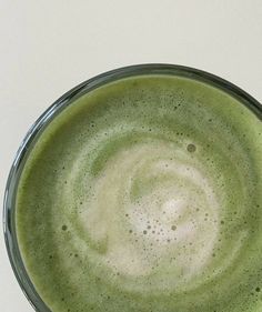 a green drink in a glass on a white table top with the bottom half filled with liquid