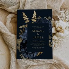 an elegant black and teal wedding card with gold foil flowers on the front is surrounded by sheer fabric