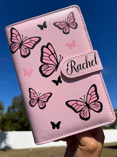 a pink wallet with butterflies on it and the name rachel written in black ink is held up by a person's hand