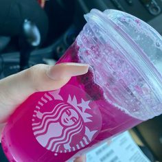 a person holding a pink starbucks cup in their left hand with the lid up and her right hand on top of it