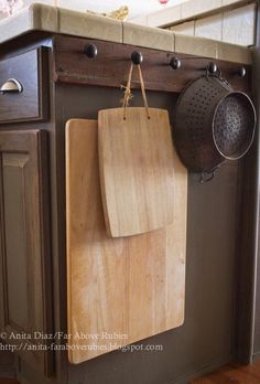 a wooden cutting board hanging from the side of a kitchen counter next to pots and pans