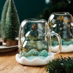 two glass mugs sitting on top of a wooden table next to christmas tree decorations