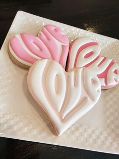 three decorated heart shaped cookies on a white plate with pink and white icing in the shape of hearts