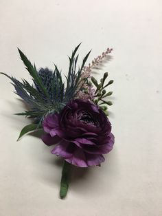 a purple flower and some green leaves on a white surface