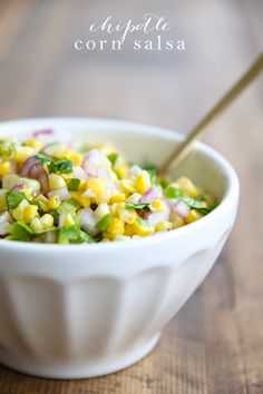 a white bowl filled with corn and green onions on top of a wooden table next to a spoon