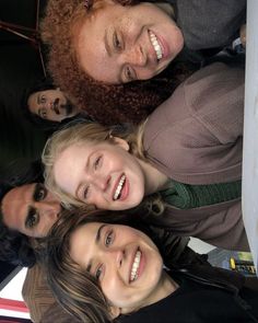 four women are standing together in a circle smiling at the camera, with their heads tilted to the side