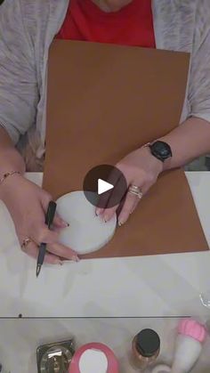 a woman is cutting paper with scissors on a white board and surrounded by other crafting supplies