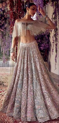 a woman in a white and gold lehenga with purple flowers on the wall