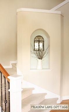 a white vase with flowers in it sitting on top of a stair case next to a window