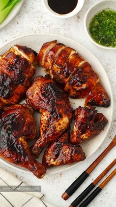 chicken wings with sauces and chopsticks on a white plate next to green onions