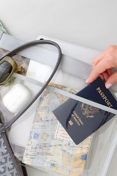 a person is holding a passport, glasses and other items on a clear table with a white bag