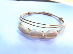 "Wire wrapped cowrie shell bangles . These are really beautiful in person, the pictures don't do them justice. They are made with tarnish resistant wire and carefully chosen cowrie shells. Can be stacked or worn alone for a dainty look. This listing is for (1) one bangle. Sizes: Child 2\" Small 2.4\" Medium 2.6\" Large 2.8 If you would like to request a custom size, please send me a message with the size you would like, and I will customize it for you. Check out our other bangles here: https://e Adjustable Gold Shell-shaped Bracelet, Gold Shell Bracelets For Gifts, Gold Shell Bracelets For Gift, Adjustable Hand Wrapped Shell Jewelry, Stackable Bangle Bracelets For The Beach, Elegant Shell Bracelet As A Gift, Elegant Shell-shaped Bracelet As A Gift, Elegant Shell-shaped Bracelet Gift, Elegant Shell-shaped Bracelet