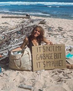 a woman sitting on the beach holding a sign that says it's not my garbage but it's my planet