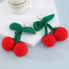 crocheted cherries hanging from the end of a pair of earrings on top of a white surface