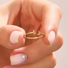 a woman's hand holding a gold ring with the letter n on it