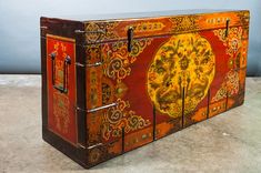 an old wooden box with decorative designs painted on the front and sides, sitting on a concrete floor