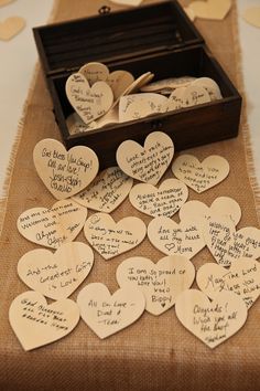 many wooden hearts with writing on them are sitting in a box next to some confetti