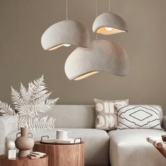 three lamps hanging from the ceiling above a couch in a room with white furniture and pillows