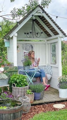 a woman sitting in a garden shed with potted plants on the porch and table