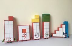 five different colored blocks with faces and eyes on them, lined up against a white wall