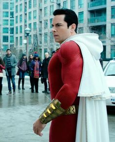 a man in a red and white costume is standing on the street with other people