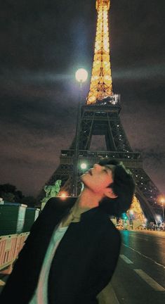 a woman standing in front of the eiffel tower at night with her eyes closed