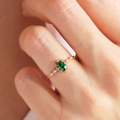 a woman's hand with a green ring on top of her finger and an emerald stone in the middle