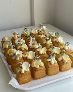 there are many small pieces of cake with flowers on them sitting on a white platter