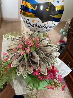 a bunch of money wrapped around a balloon with congratulations written on it and flowers in the center