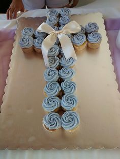 a cross made out of cupcakes on top of a cake sheet with a ribbon