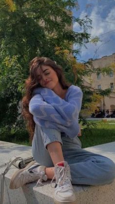 a young woman sitting on the edge of a cement wall with her hands behind her head