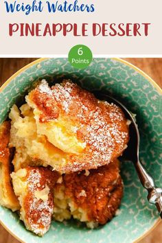 a blue bowl filled with pineapple dessert next to a fork and cup full of powdered sugar