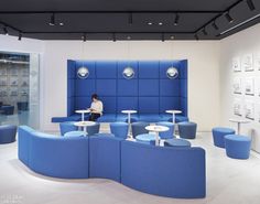 a person sitting on a blue couch in a room with white tables and stools