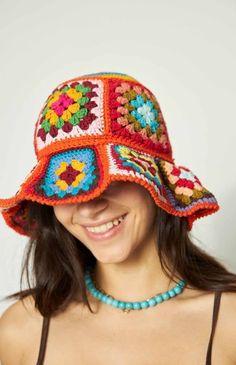 a woman wearing a colorful crocheted hat with flowers on the brim, smiling