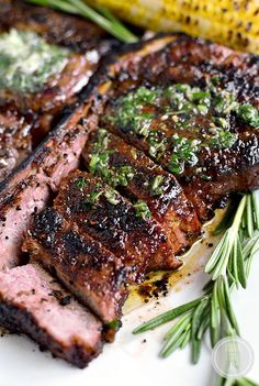 grilled steak with herbs on a plate next to a corn cob and green garnish