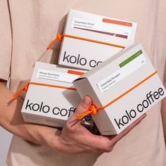 the person is holding three boxes of kolo cofee in their hands with orange string around them