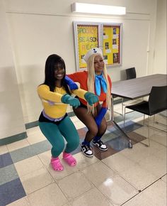 two women dressed in costumes pose for a photo while sitting on a chair at a table