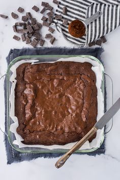 a chocolate cake in a glass pan on top of a table next to a knife