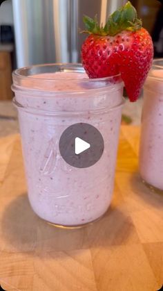 two jars filled with yogurt sitting on top of a wooden table next to a strawberry