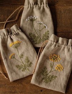 three bags with embroidered flowers on them sitting on top of a wooden table next to each other